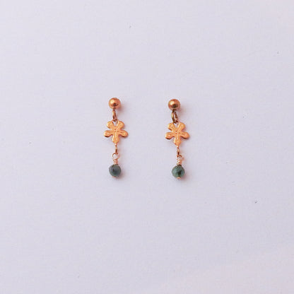 A pair of small gold-toned dangle earrings with a flower-shaped charm and a green bead drop, shown on a plain light background.