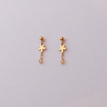 A pair of small gold dangle earrings with a flower-shaped charm, a tiny gold bead above, and a dangling faceted bead, shown on a plain light background.