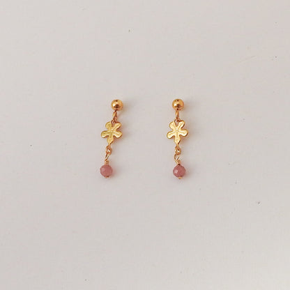 A pair of gold dangle earrings with a small flower charm and a pink bead drop, displayed on a plain light gray background.