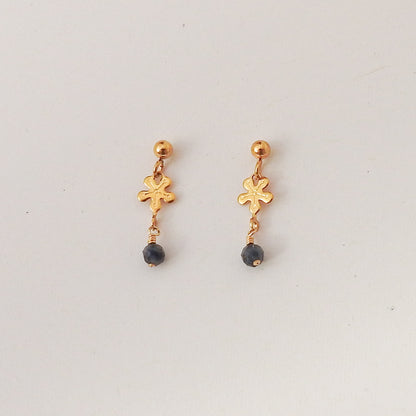 A pair of gold dangle earrings with a small textured cross charm and a dark gray bead drop, shown on a plain light gray background.