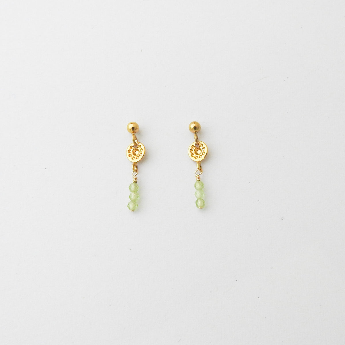 A pair of gold dangle earrings with ornate circular charms and small light green bead drops, displayed on a clean white background.