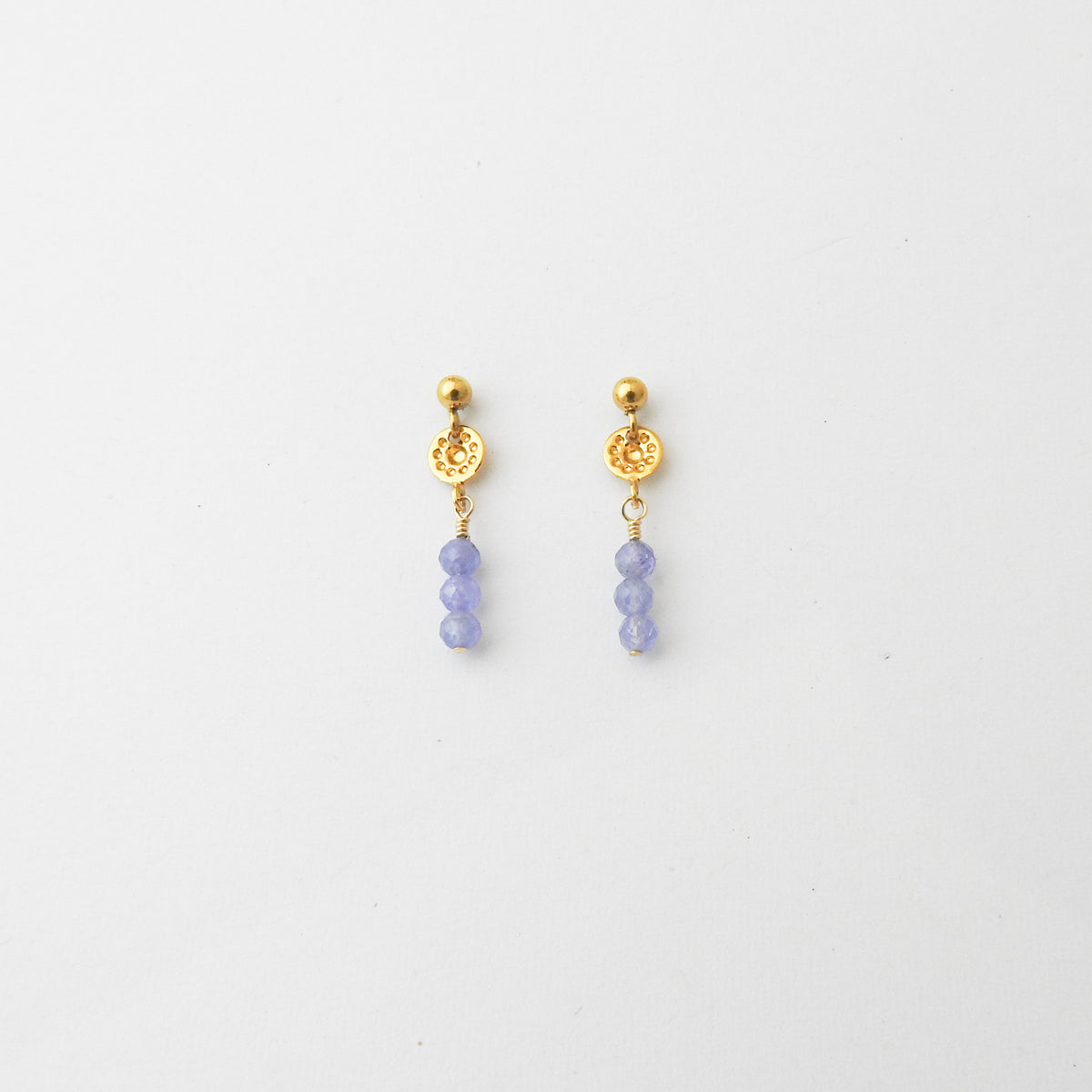 A pair of gold dangle earrings with textured circular charms and three small lavender-blue beads hanging below, shown on a plain white background.