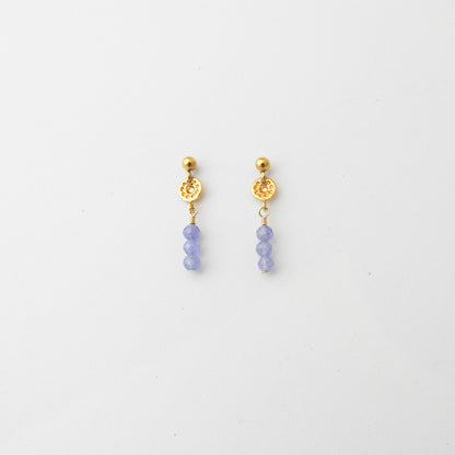 A pair of gold dangle earrings with textured circular charms and three small lavender-blue beads hanging below, shown on a plain white background.