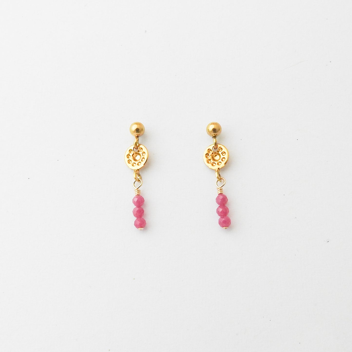 A pair of gold drop earrings with a textured circular disc, a small gold bead, and three dangling pink beads, shown on a plain white background.