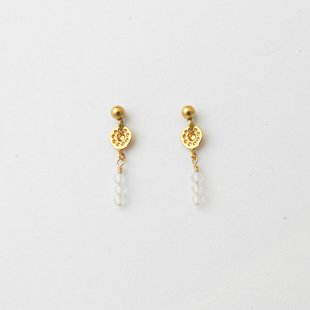 A pair of gold-toned dangle earrings with circular filigree details and small clear bead drops, shown on a plain white background.
