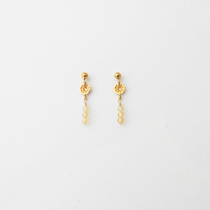 A pair of gold dangle earrings with a textured circular disc, a small gold bead, and three pale yellow beads hanging below, shown on a plain white background.