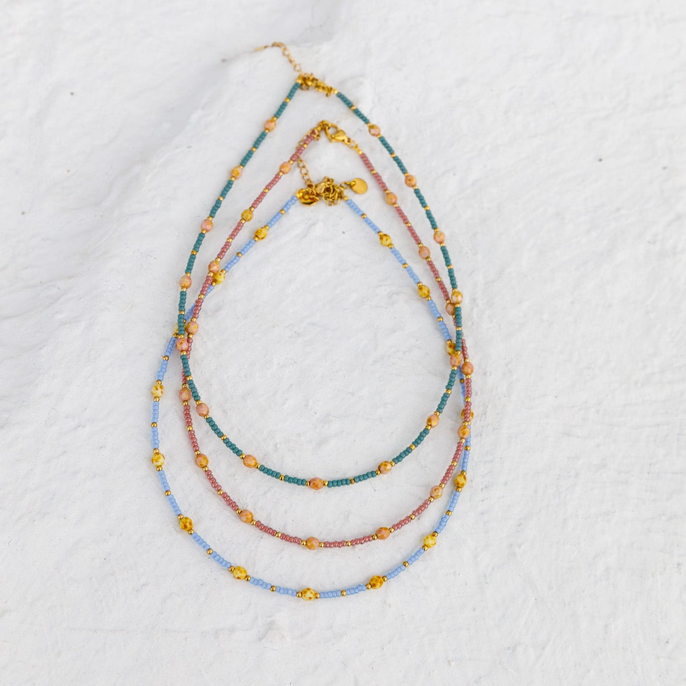 Set of three beaded necklaces on a textured white surface