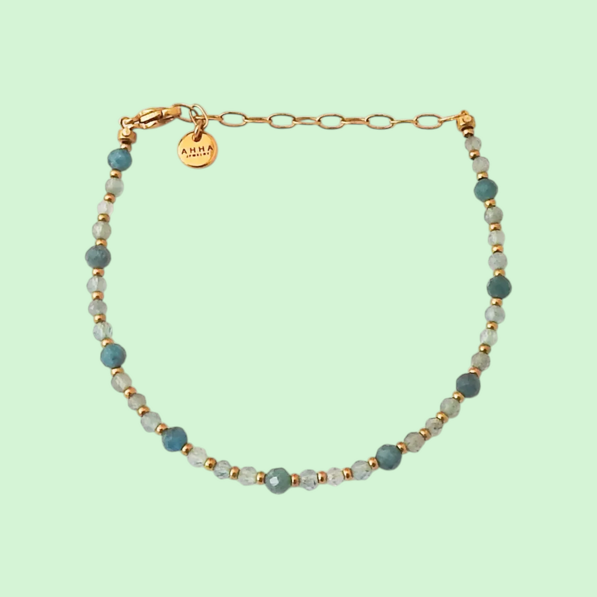 A beaded necklace featuring gray and dark blue faceted beads with a gold-tone shell pendant, displayed on a solid pale mint green background.