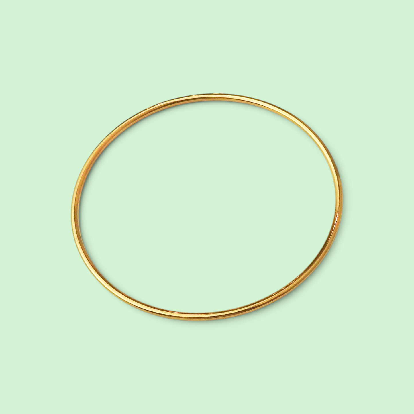 A thin, polished gold bangle bracelet shown against a solid pale mint green background.
