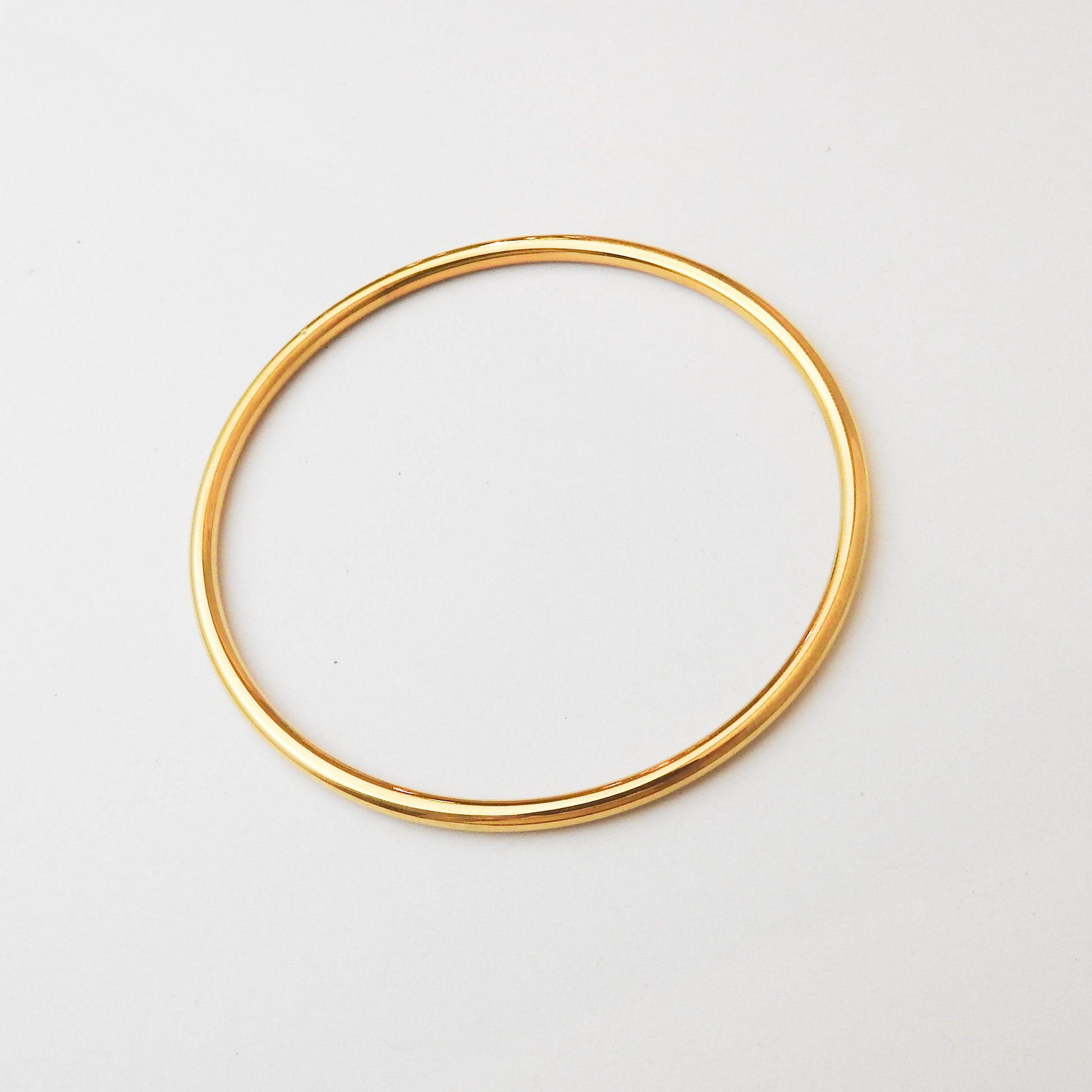 A thin, polished gold bangle bracelet shown on a clean, light off-white background.