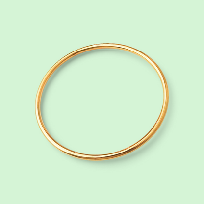 A thin, polished gold bangle bracelet shown against a solid pale mint green background.