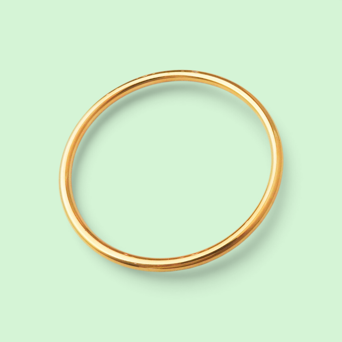 A simple polished gold bangle bracelet shown on a solid pale mint green background.