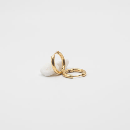 A single gold stud earring with a clear gemstone, shown in profile against a solid off-white background.