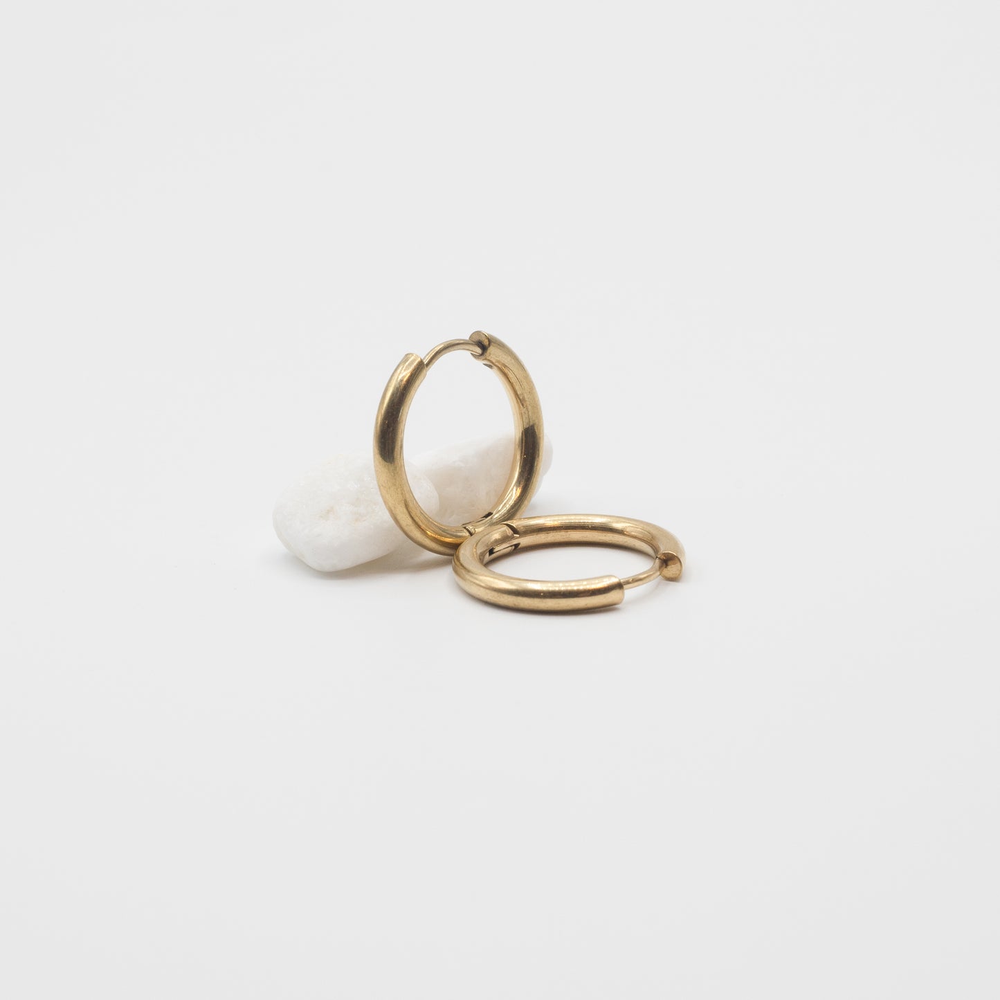 A pair of small gold hoop earrings displayed on a white stone against a clean white background.