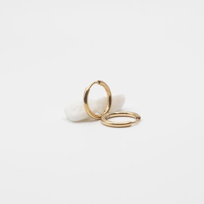 Two thin gold hoop earrings resting on a small white stone against a clean white background.