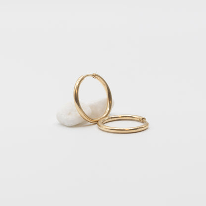 Two thin gold hoop earrings resting on a small white stone against a clean white background.