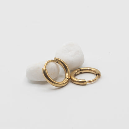 Two small gold hoop earrings resting on two smooth white stones against a clean white background.