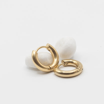 A pair of gold huggie hoop earrings displayed on small white stones against a clean white background.