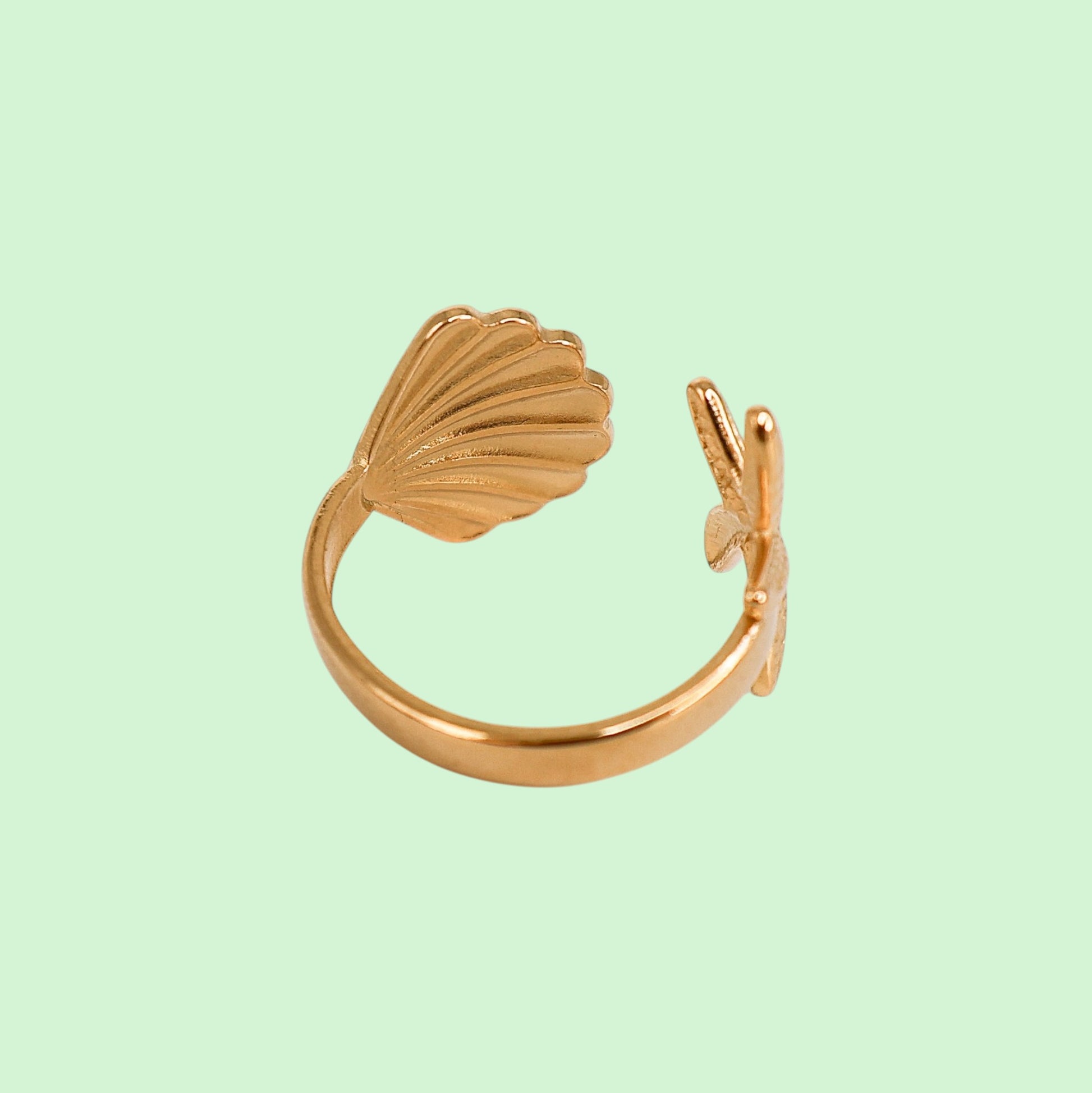 Gold shell-shaped ring on a light green background