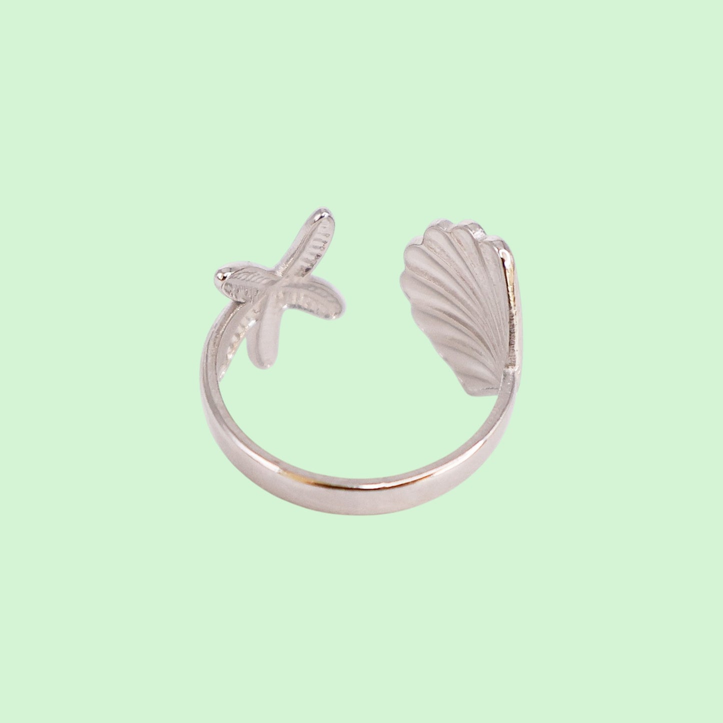 Silver ring with shell and starfish design on a light green background