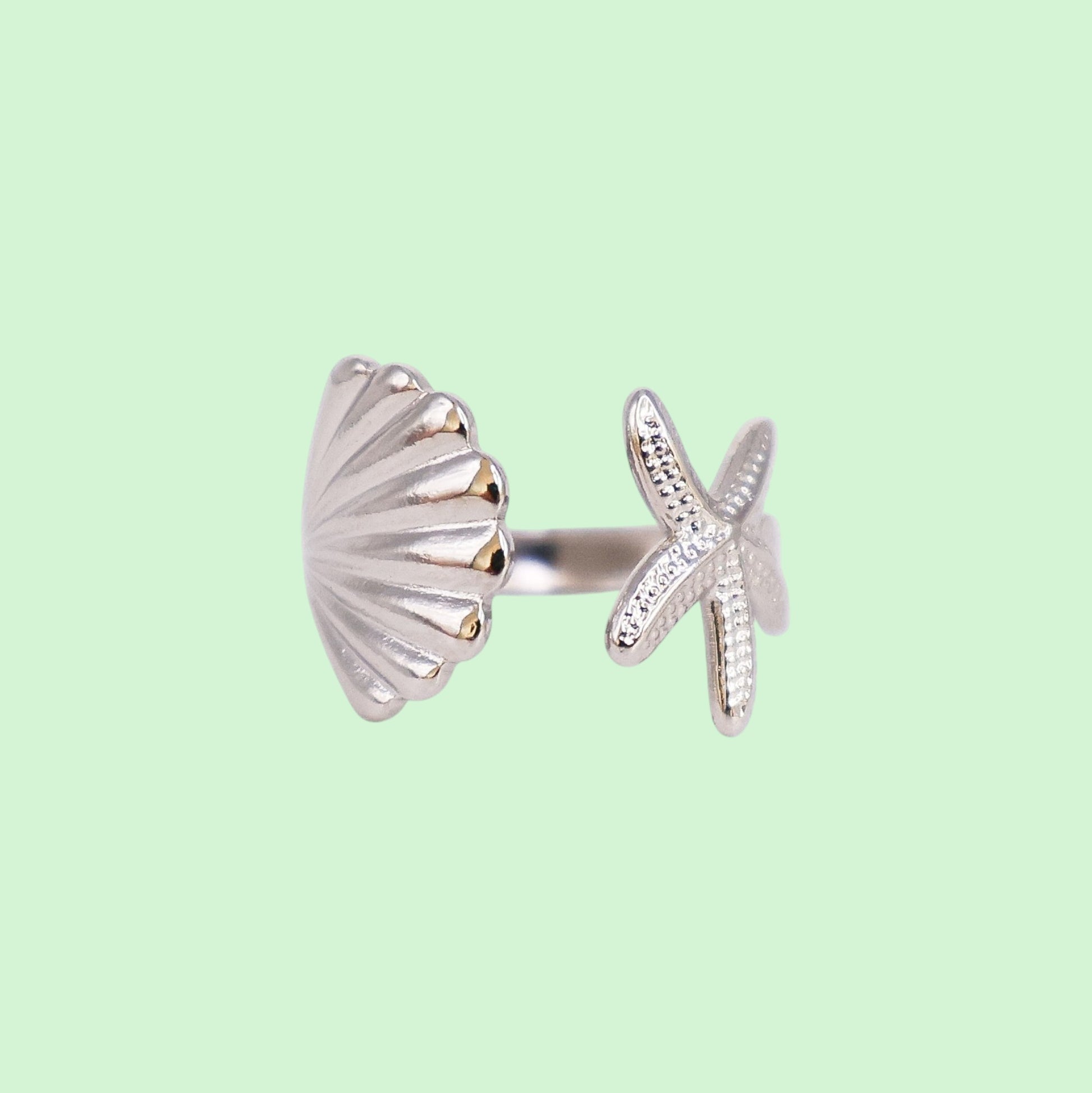 Silver ring with shell and starfish design on a light green background