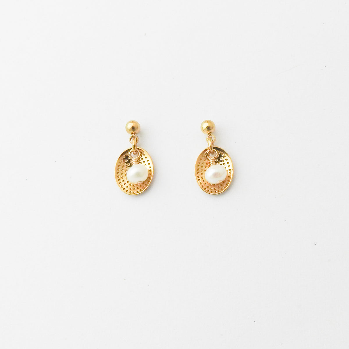 A pair of gold-toned dangle earrings with textured oval drops and white pearl-like center beads, shown on a plain white background.