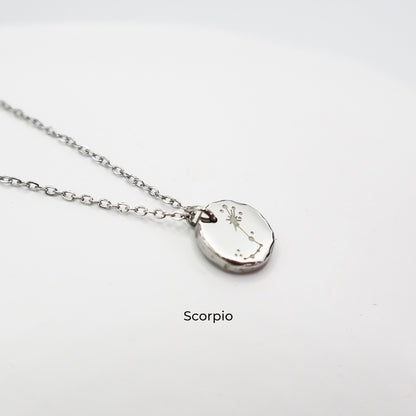 Silver necklace with a round pendant on a light gray background. The pendant is engraved with the Scorpio star sign constellation