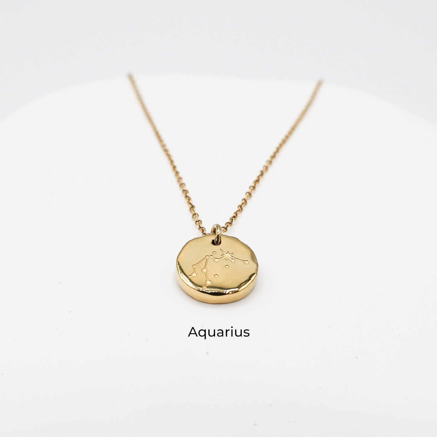 Gold necklace with a round pendant on a light gray background. The pendant is engraved with the Aquarius star sign constellation