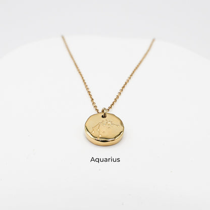 Gold necklace with a round pendant on a light gray background. The pendant is engraved with the Aquarius star sign constellation