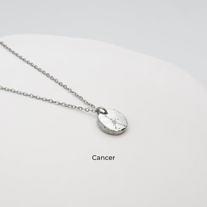 Silver necklace with a round pendant on a light gray background. The pendant is engraved with the Cancer star sign constellation