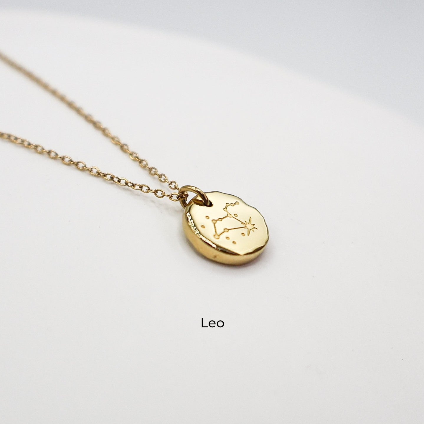 Gold necklace with a round pendant on a light gray background. The pendant is engraved with the Leo star sign constellation