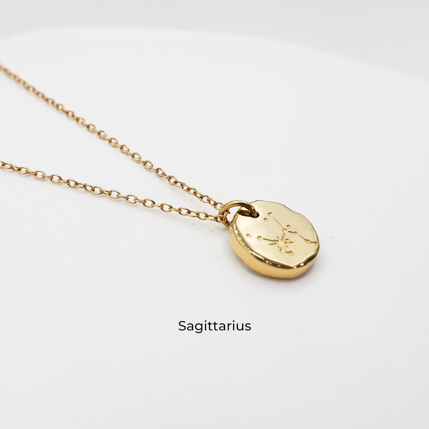 Gold necklace with a round pendant on a light gray background. The pendant is engraved with the Sagittarius star sign constellation