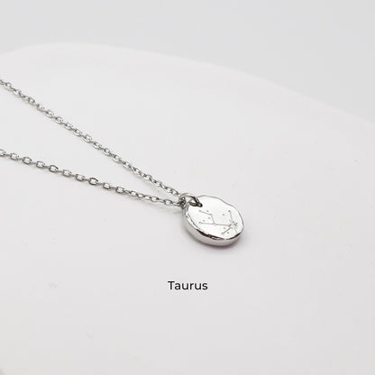 Silver necklace with a round pendant on a light gray background. The pendant is engraved with the Taurus star sign constellation