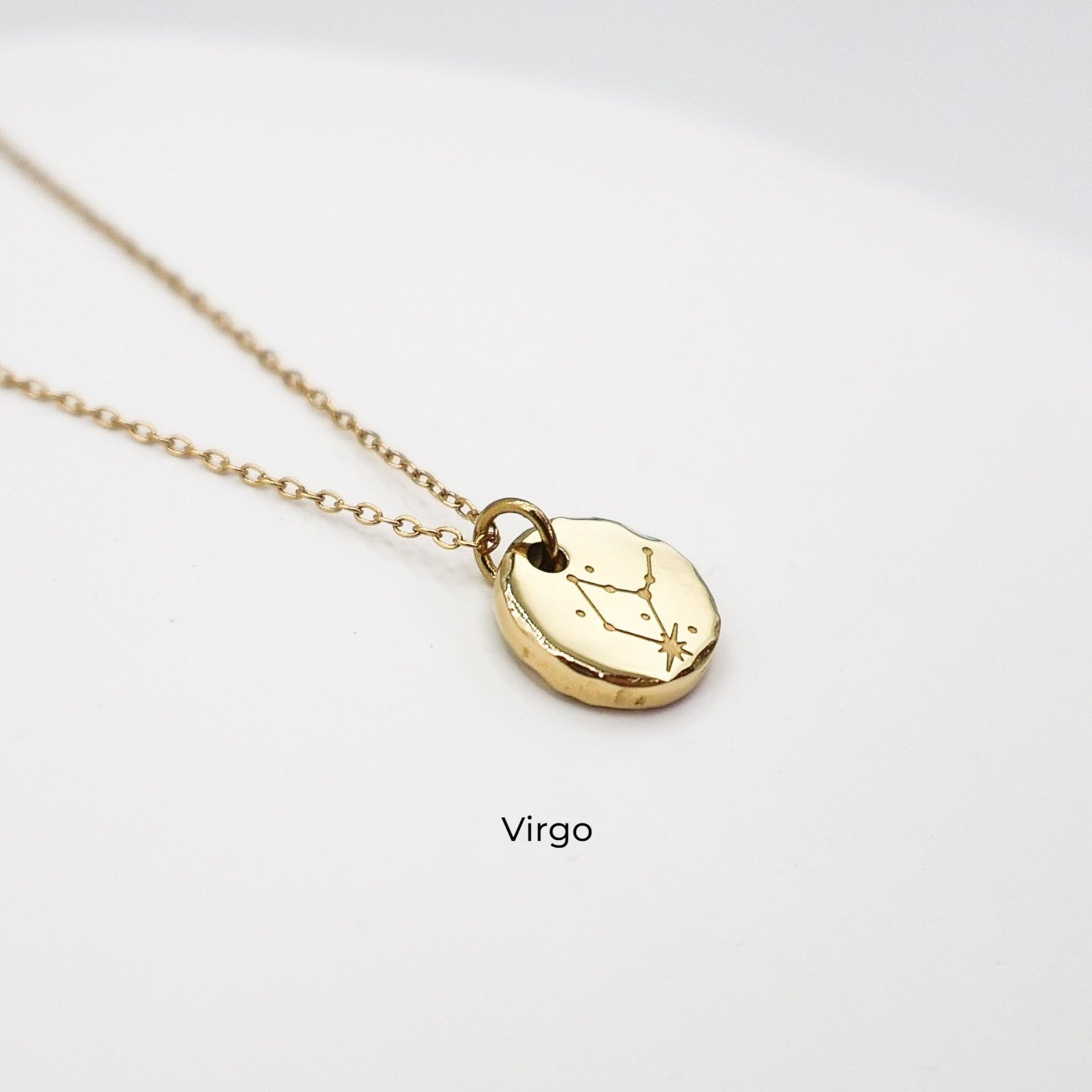 Gold necklace with a round pendant on a light gray background. The pendant is engraved with the Virgo star sign constellation
