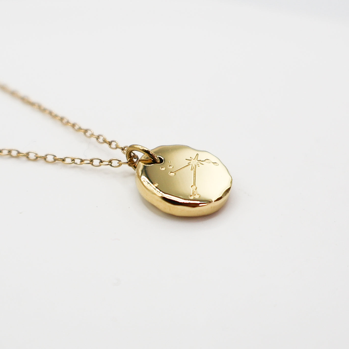 Gold necklace with a round pendant on a light gray background. The pendant is engraved with the Aries star sign constellation