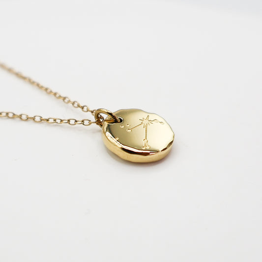 Gold necklace with a round pendant on a light gray background. The pendant is engraved with the Aries star sign constellation
