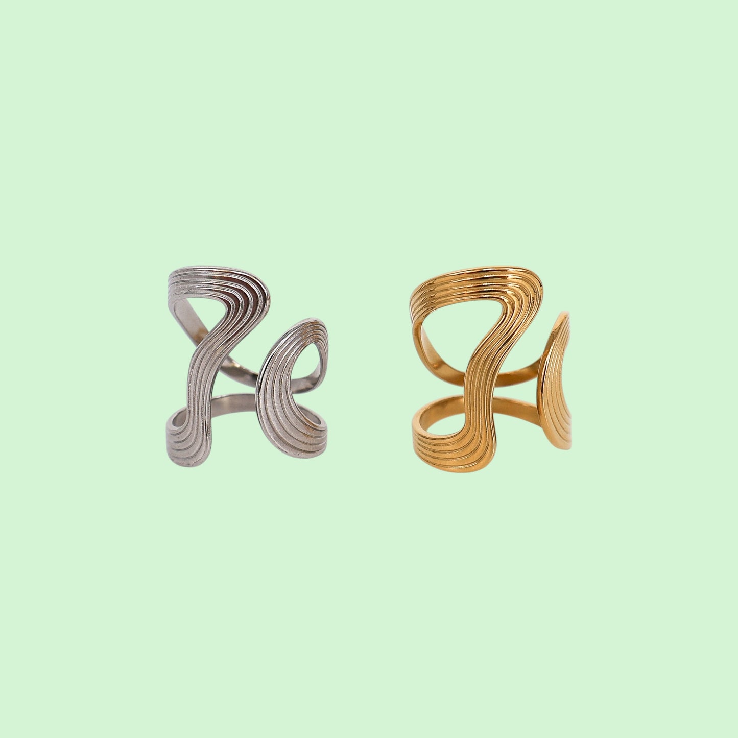 Two metallic ring holders, one silver and one gold, on a light green background.
