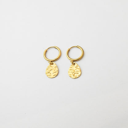 A pair of small gold huggie hoop earrings with textured teardrop charms, displayed on a clean white background.