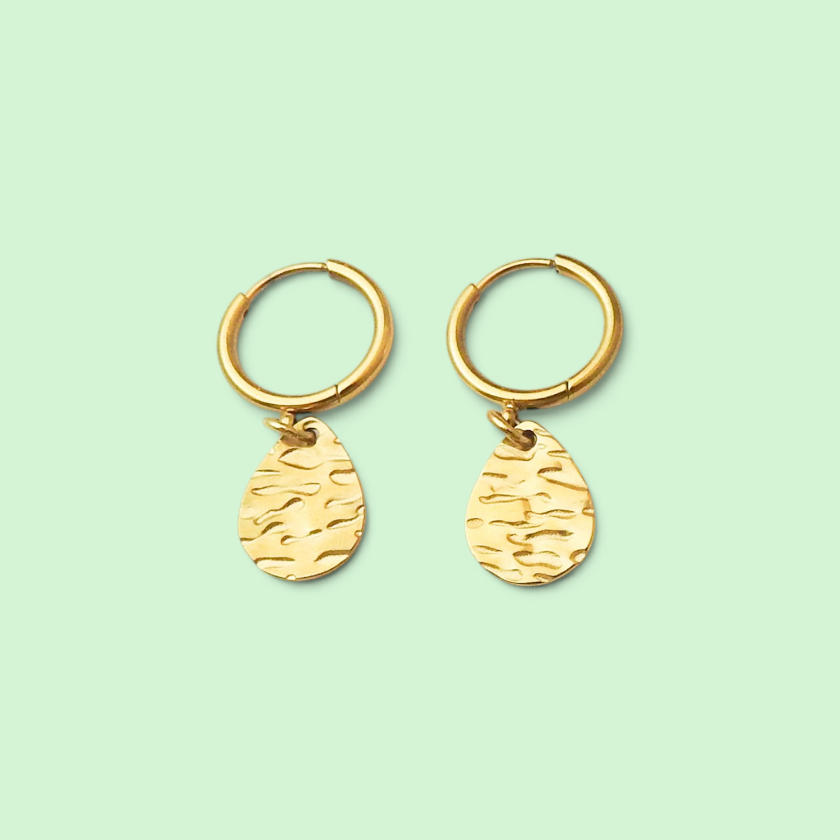 A pair of gold hoop earrings with textured teardrop charms, displayed on a solid pale mint green background.