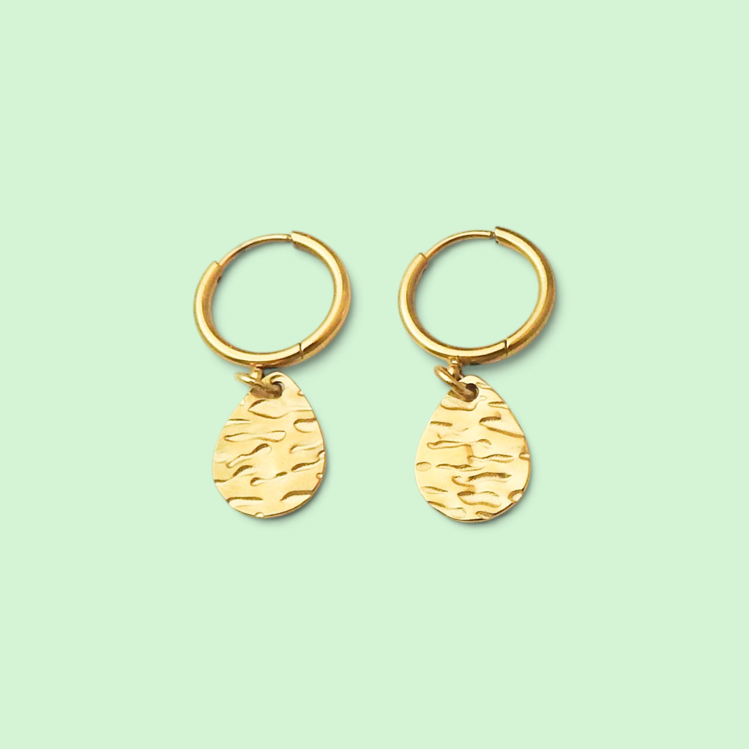A pair of gold hoop earrings with textured teardrop charms, displayed on a solid pale mint green background.
