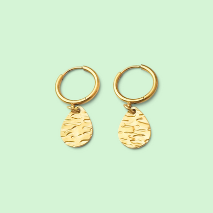A pair of gold hoop earrings with textured teardrop charms, displayed on a solid pale mint green background.