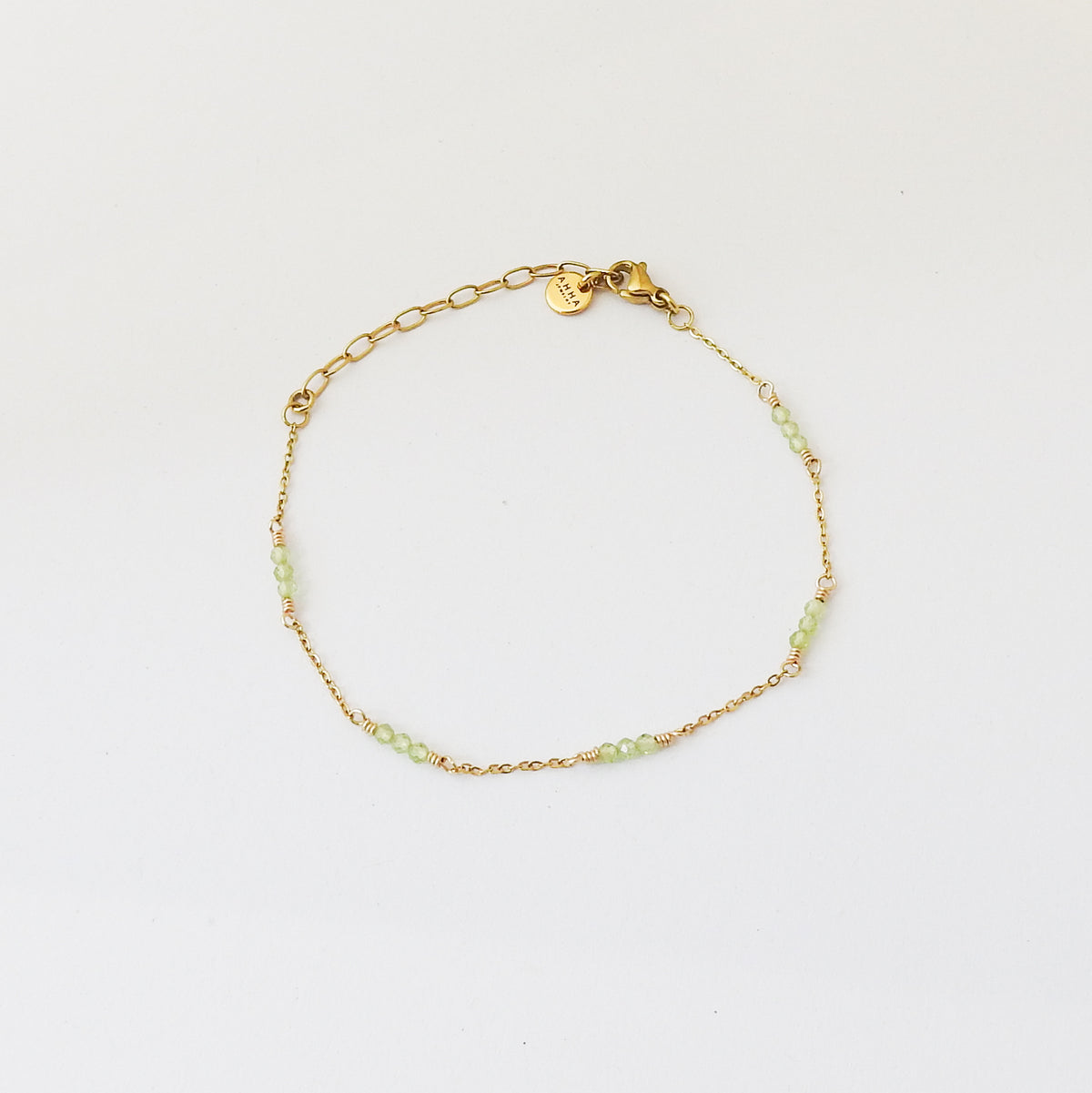 A delicate gold chain bracelet with small light green beads spaced along the front, displayed on a clean white background.