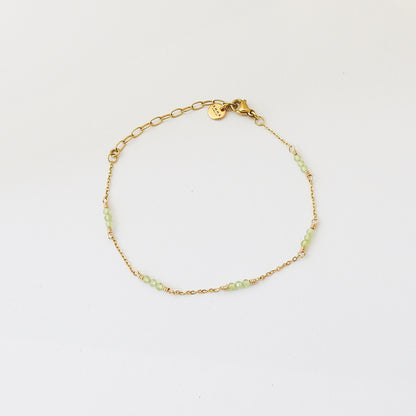 A delicate gold chain bracelet with small light green beads spaced along the front, displayed on a clean white background.