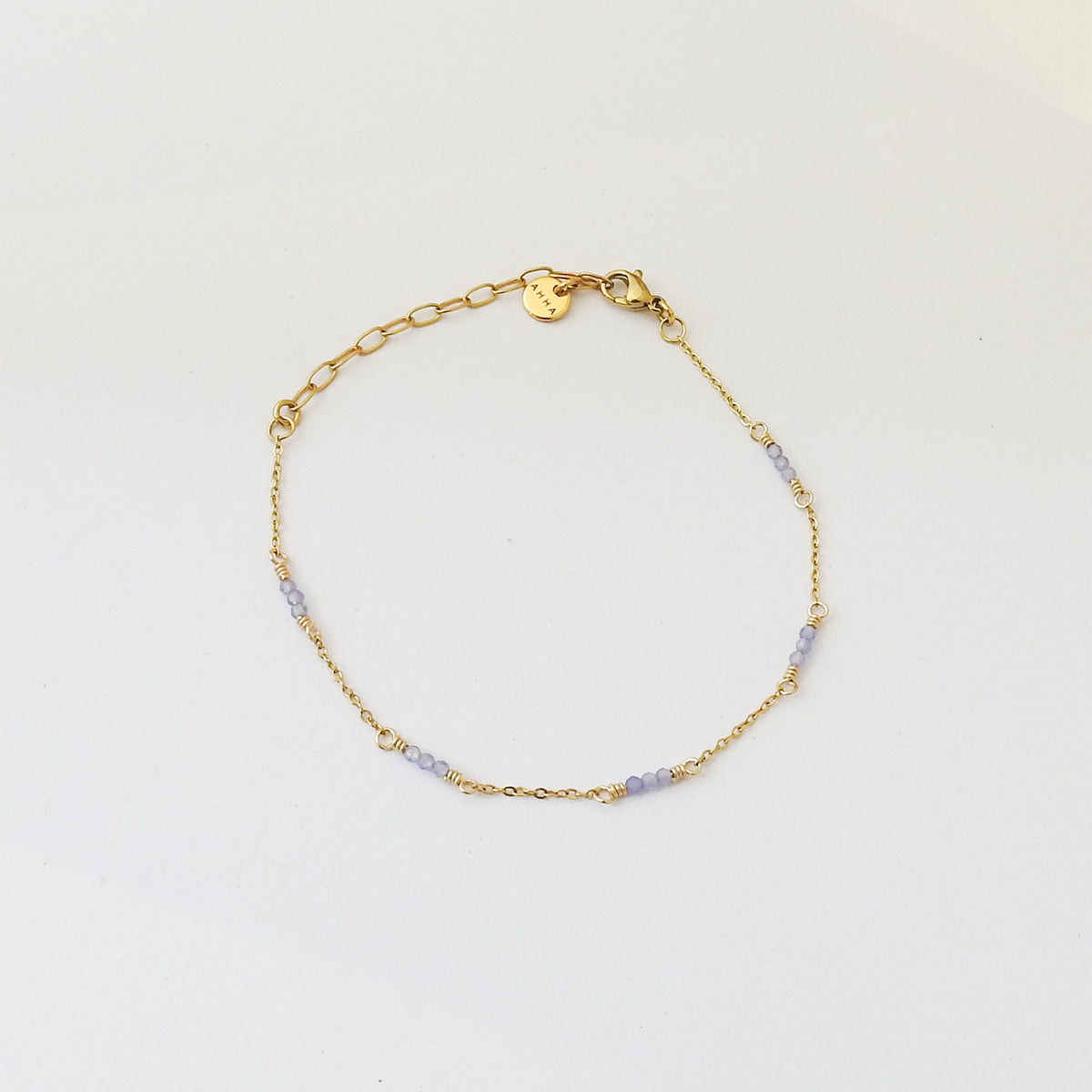 A delicate gold chain bracelet with small light purple beads spaced along the chain, displayed on a clean white background.