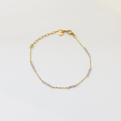 A delicate gold chain bracelet with small light purple beads spaced along the chain, displayed on a clean white background.
