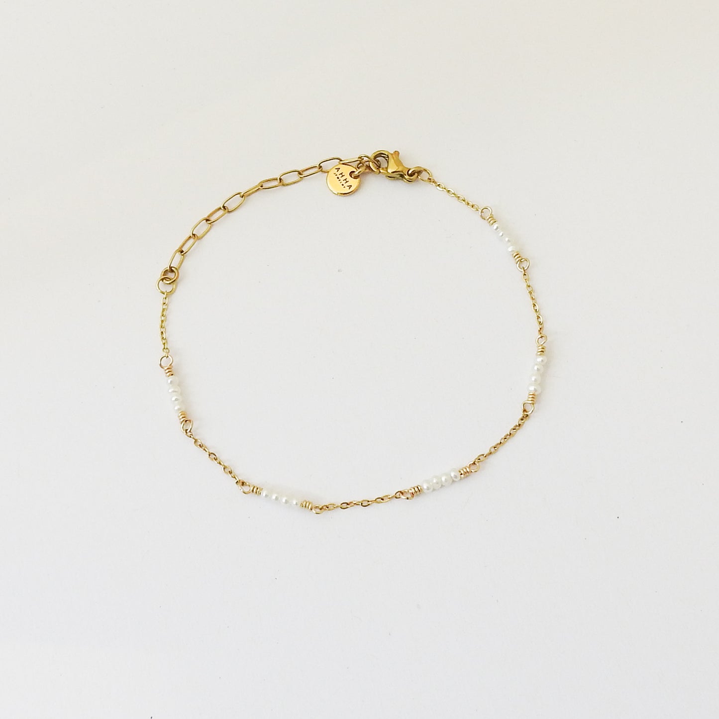 A delicate gold chain bracelet with small white pearl-like beads and a heart-shaped charm engraved with 'K', displayed on a clean white background.