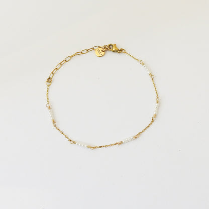 A delicate gold chain bracelet with small white pearl-like beads and a heart-shaped charm engraved with 'K', displayed on a clean white background.