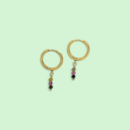 A pair of gold hoop earrings with small dangling beaded charms, shown on a solid pale mint green background.