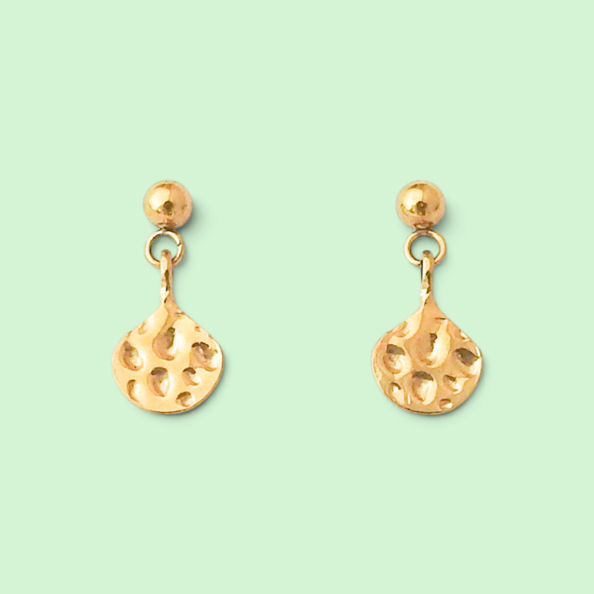 A pair of gold dangle earrings with textured teardrop-shaped drops and small round studs, shown on a solid pale mint green background.