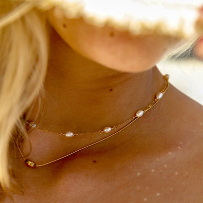 A close-up image of a woman's neck wearing a delicate gold necklace with freshwater pearls.